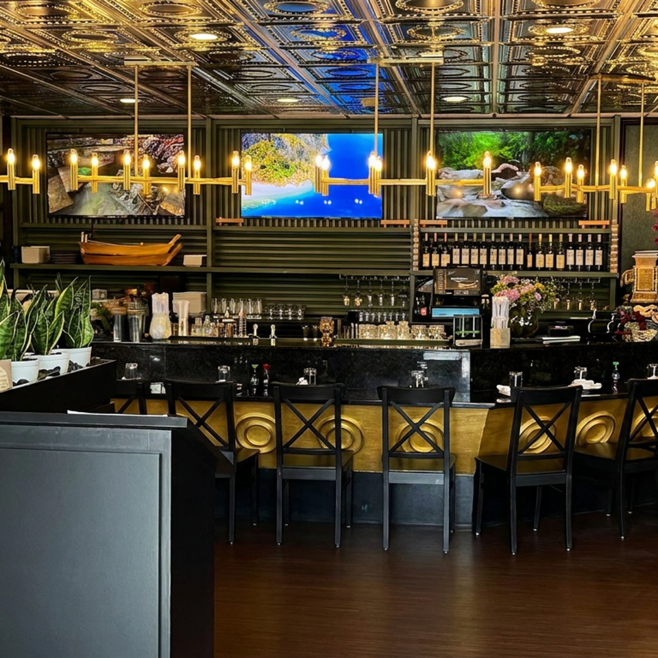Elegant restaurant bar with gold accents, illuminated chandelier ceiling, wine bottles, orchids, plants, and black dining chairs.